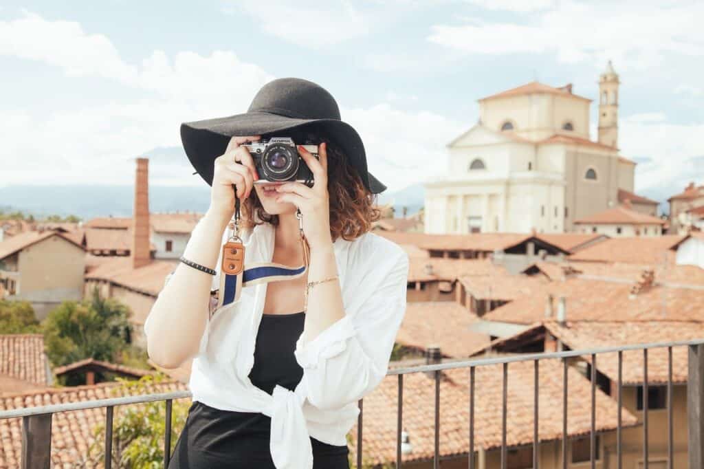 A woman holding a camera to her face with the backdrop of buildings behind her.