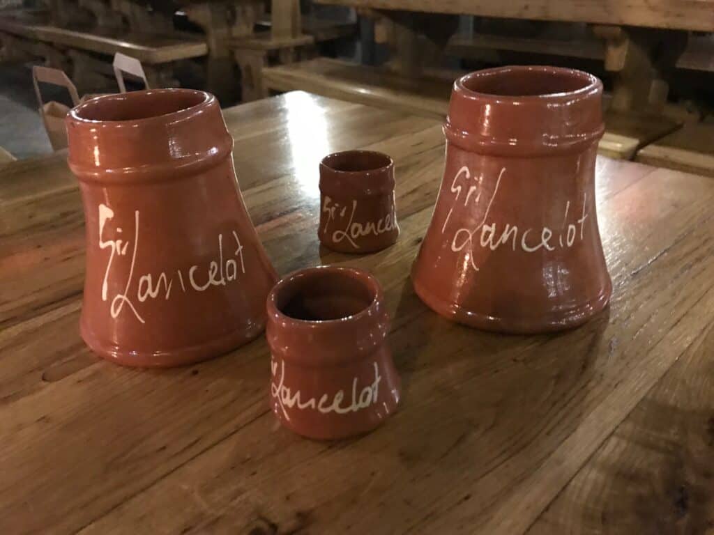 Brown, ceramic mugs with Sir Lancelot written on them sit atop a wooden table. 