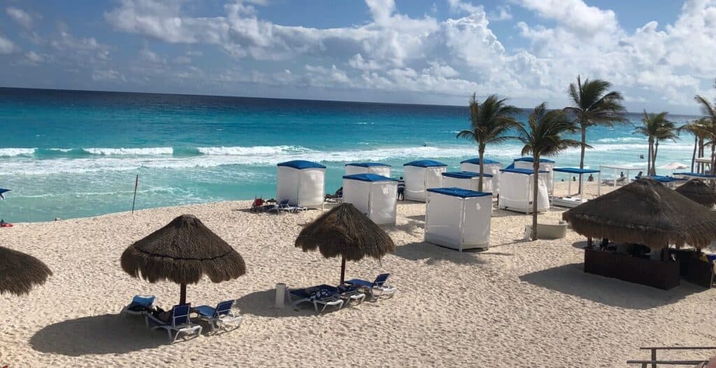A beach with crystal blue water with palm trees and cabanas at hotel in Cancun, Mexico during Covid-19 pandemic