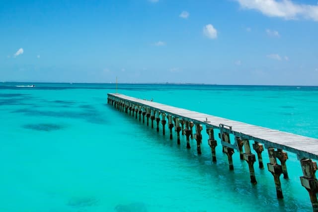 A wooden bridge jutting out into calm, turquoise blue water. 