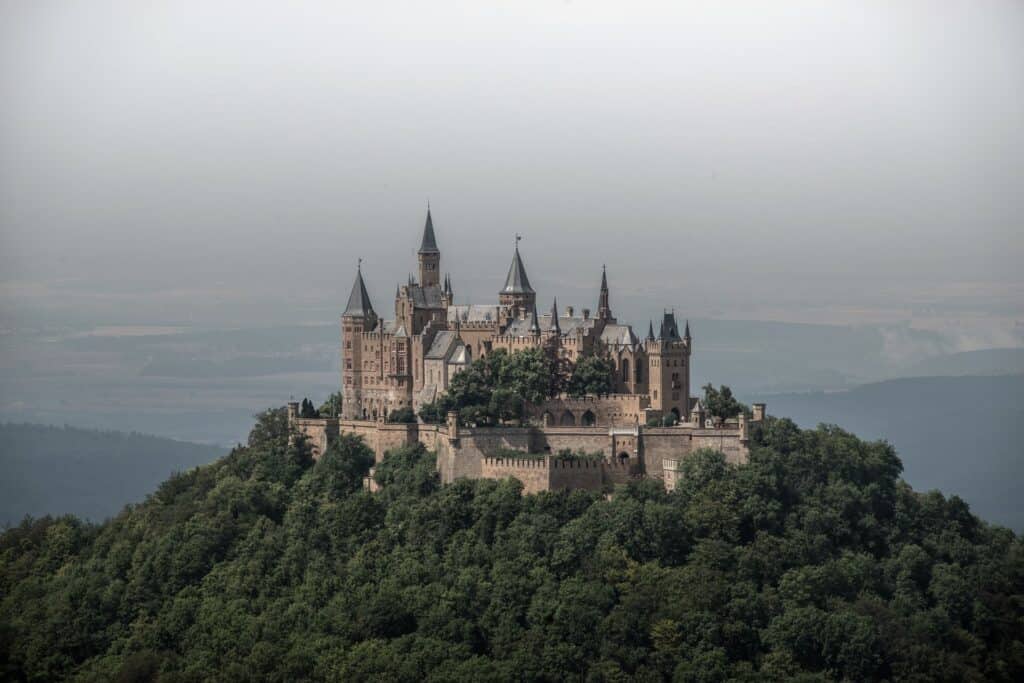 overcast skies and lush greenery surround the beautiful, neo-gothic Hohenzollern castle perched high on the mountains.