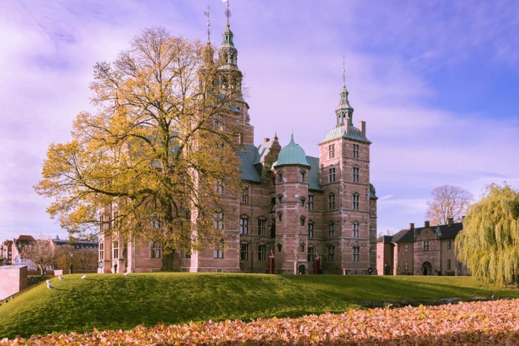 A tree bursting with autumn colors standing tall in front of the regal, royal Rosenborg castle. 