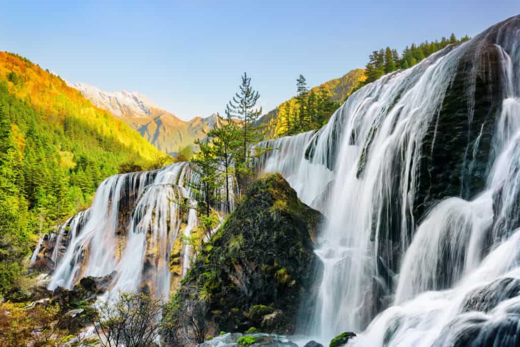 Wonderful view of the Pearl Shoals Waterfall among scenic wooded mountains and evergreen forest in Jiuzhaigou nature reserve (Jiuzhai Valley National Park), China. Amazing autumn landscape at sunset.