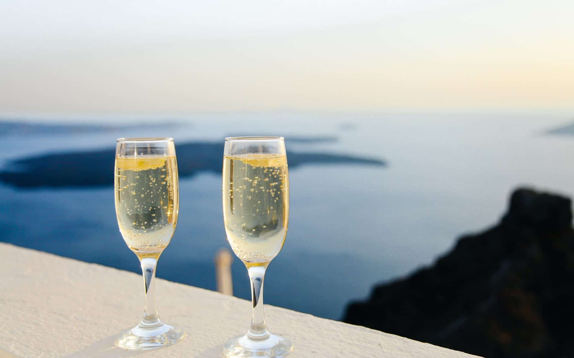 Two glasses filled with bubbly champagne on a ledge overlooking the water. 